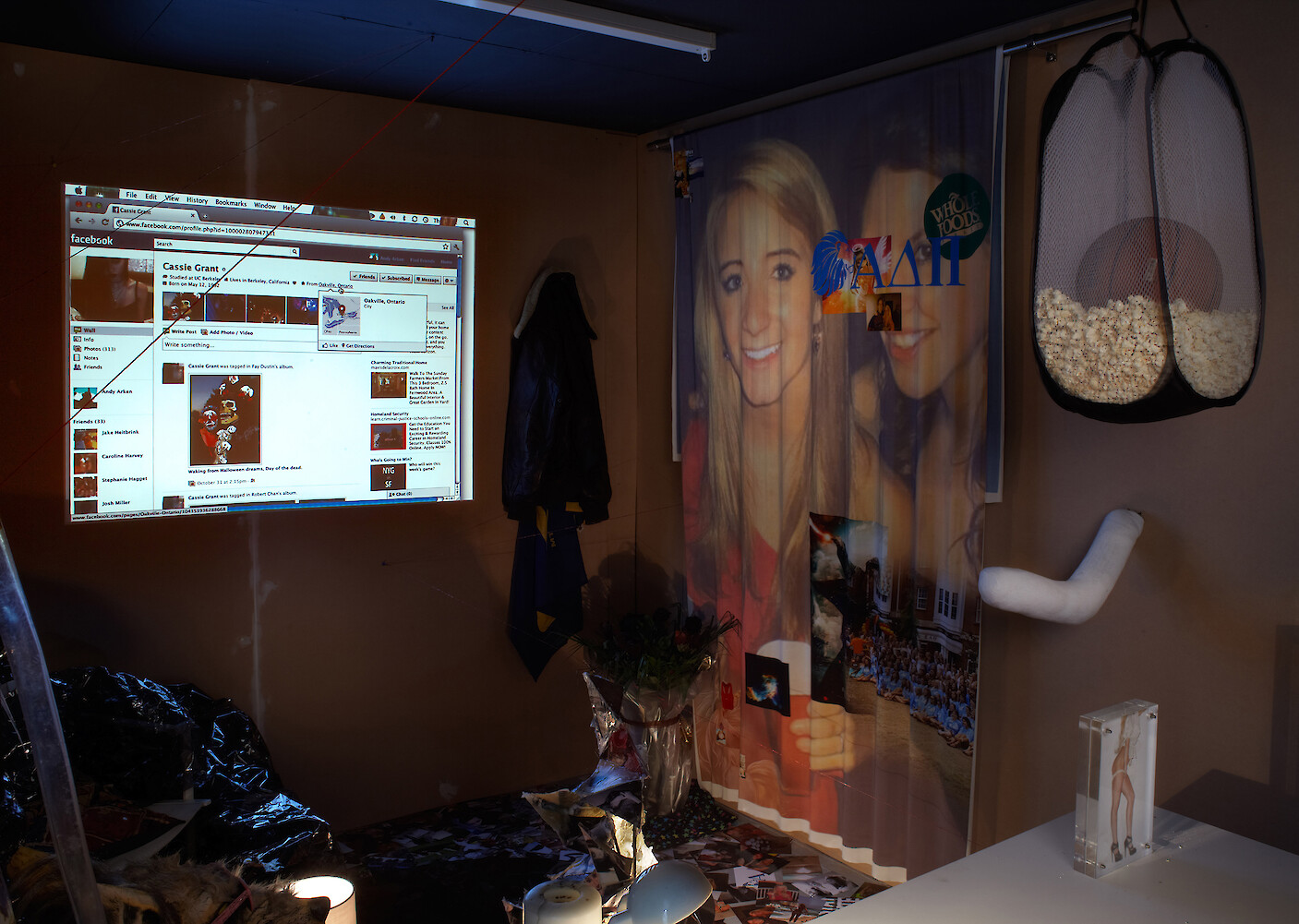 Ed Fornieles, *Dorm Daze*, 2011, Dorm Daze Facebook sitcom, Dorm Daze sitcom photographs, script book, Magic Johnson poster, red NYC cap, sports socks, steel pentagram, glass, silk jersey, computer, projector, popcorn, basketball, pinboard, jacket, voodoo doll